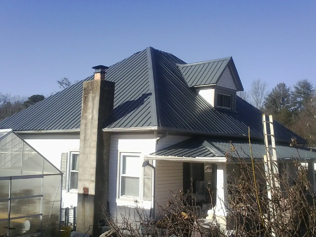 Dark blue standing seam metal roof on a white farmhouse with dormer — Slate & Tile Roof Repair by Roofing Brothers in Clark Mills