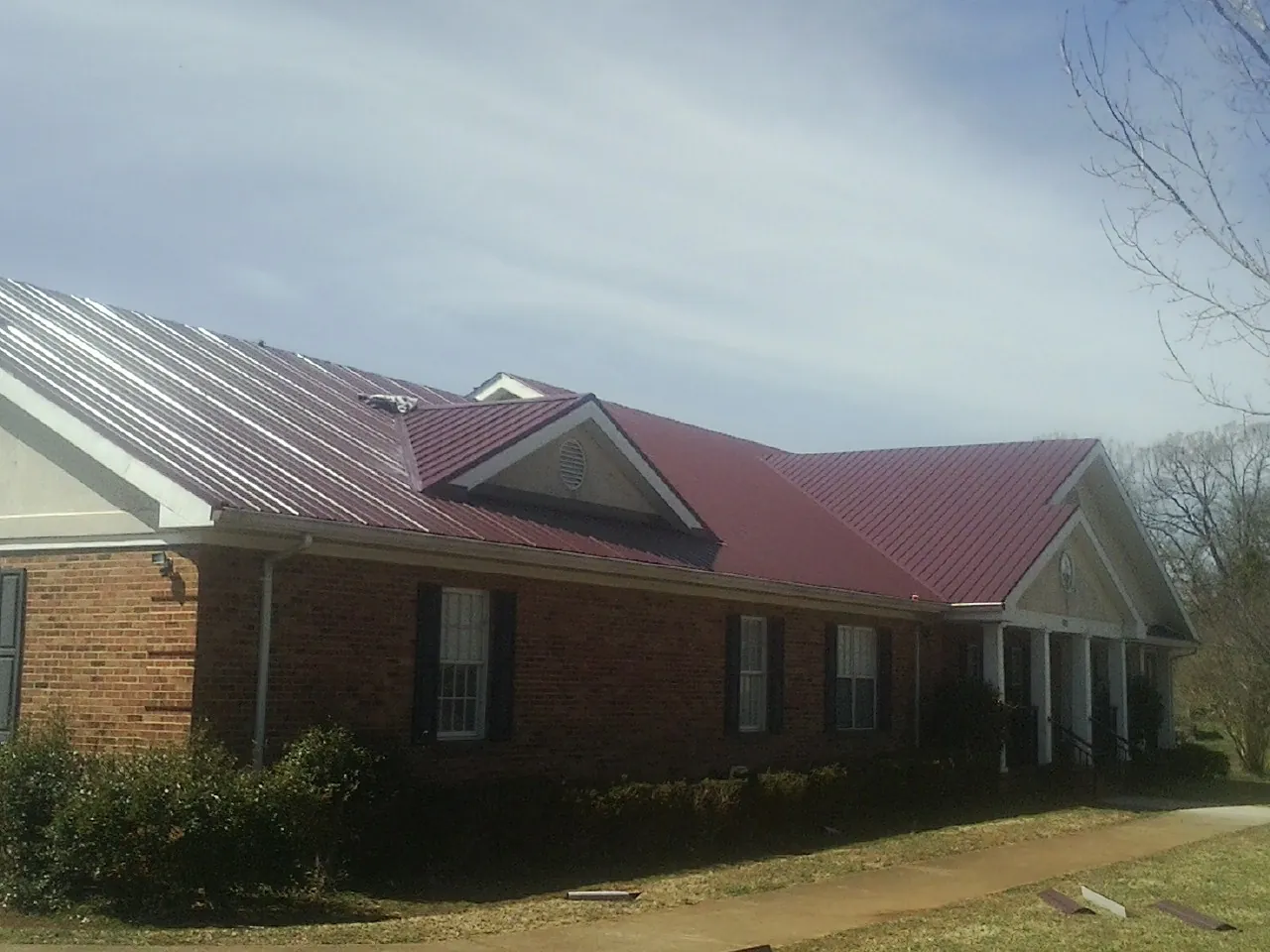 Red metal roof with gabled entries on a long brick building, from a Hail Damage Roof Repair job in Clark Mills