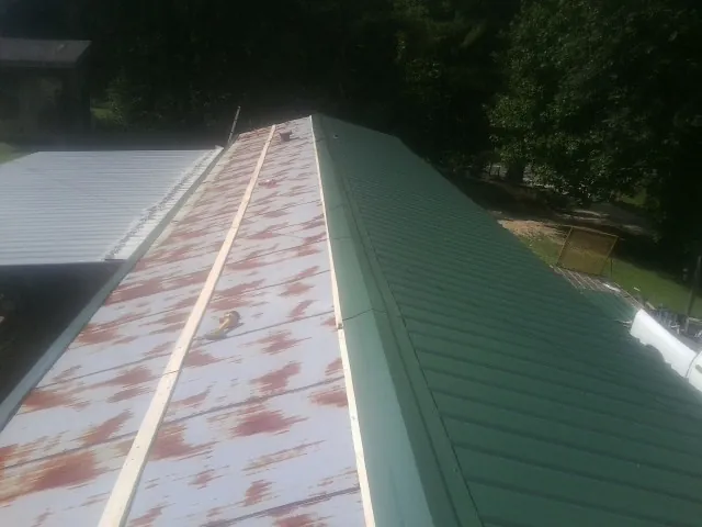 Old rusted panels beside newly installed green metal roofing — Wind Damage Roof Repair by Roofing Brothers in Clark Mills