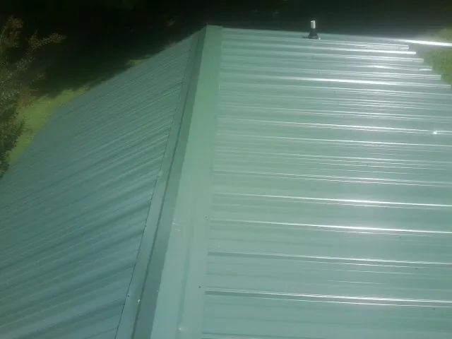 New green metal panels meeting at the ridge of a roof — Flat Roof Repair work by our crew in Clark Mills
