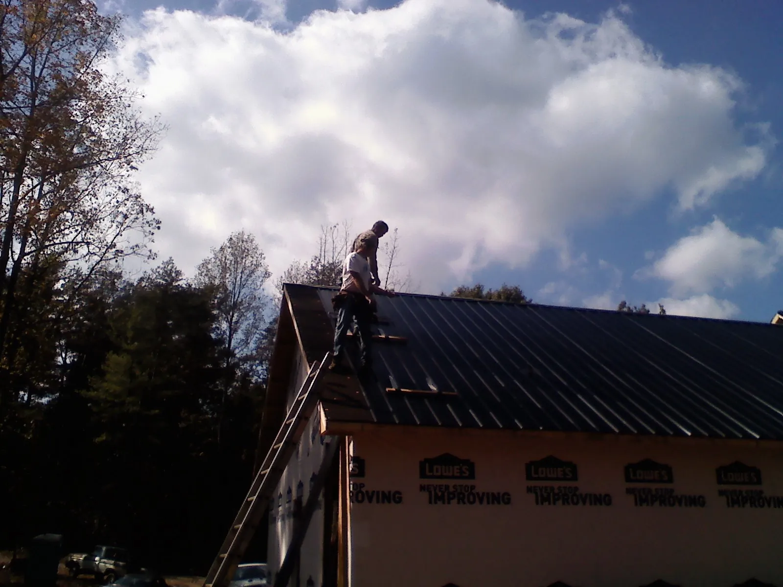 Roofer fastening dark metal panels high against a cloudy sky, from a Roof Inspection job in Clark Mills