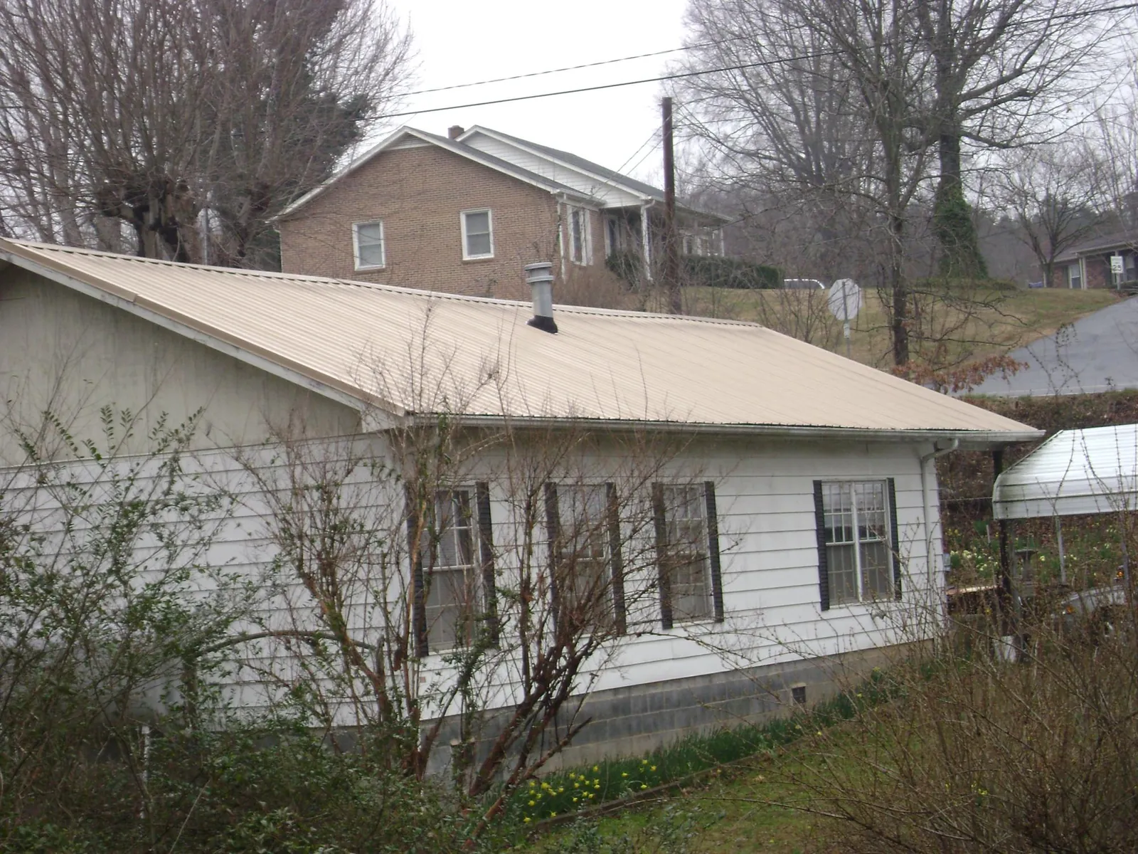Tan metal roof on a white sided house set into a hillside — Commercial Roofing by Roofing Brothers in Clark Mills