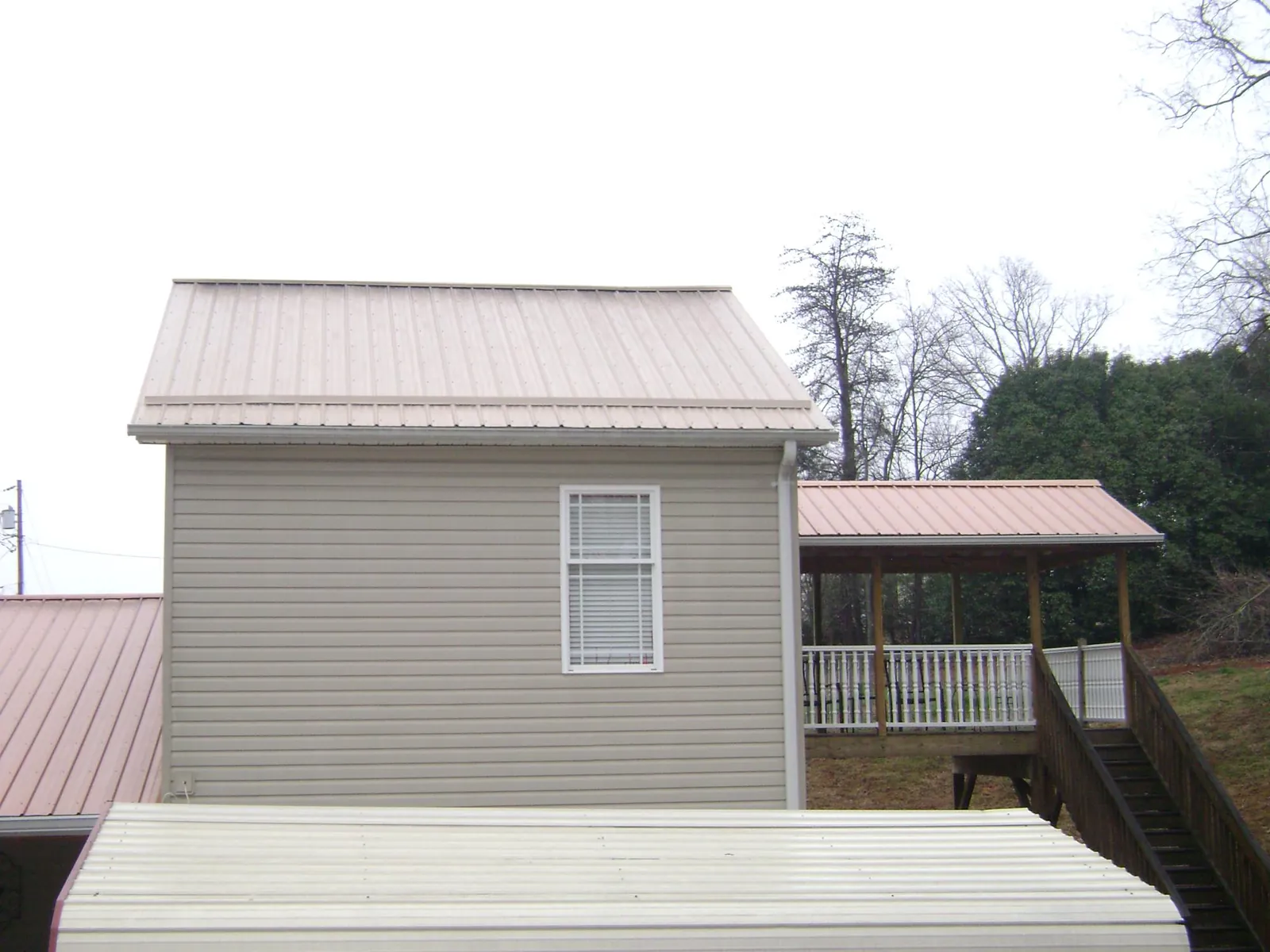 Tan metal roofs on a two story addition and attached porch, from a Roof Replacement job in Clark Mills